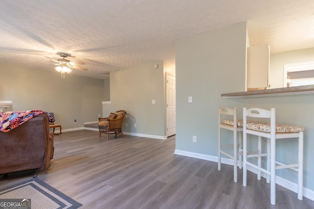 living area with a ceiling fan, wood finished floors, baseboards, and a textured ceiling