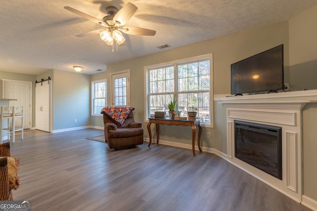 living area featuring wood finished floors, visible vents, ceiling fan, a textured ceiling, and a barn door