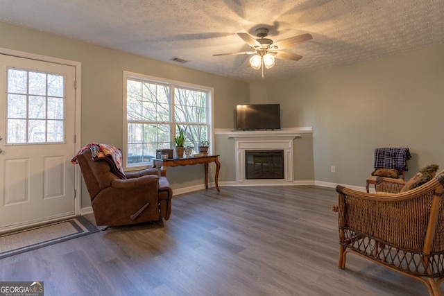 sitting room with a ceiling fan, wood finished floors, visible vents, a textured ceiling, and a glass covered fireplace