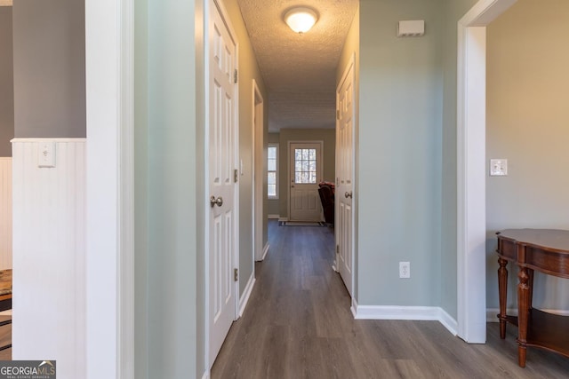 hall featuring baseboards, a textured ceiling, and dark wood-style flooring