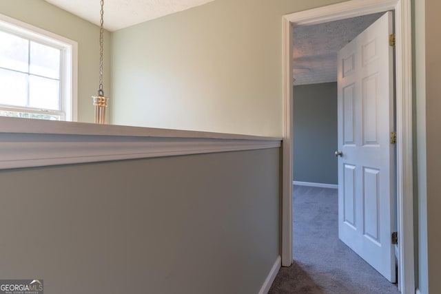 hall with dark colored carpet, baseboards, and a textured ceiling