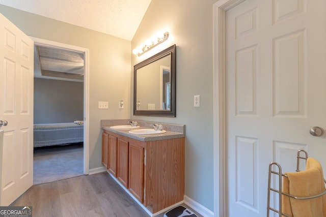 ensuite bathroom featuring a sink, ensuite bath, wood finished floors, and vaulted ceiling