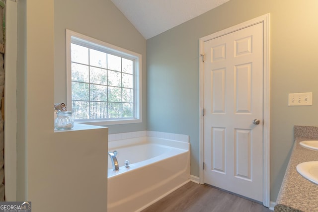 full bathroom with vanity, lofted ceiling, a garden tub, and wood finished floors