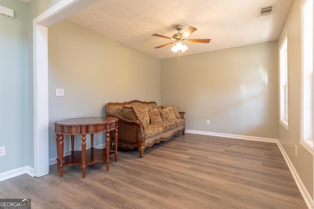 sitting room featuring wood finished floors, visible vents, baseboards, ceiling fan, and a textured ceiling