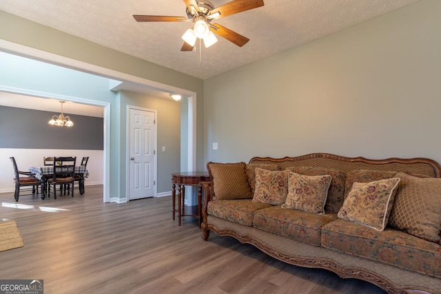 living room featuring lofted ceiling, ceiling fan with notable chandelier, a textured ceiling, wood finished floors, and baseboards