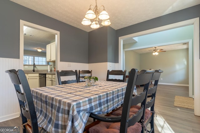 dining space featuring a textured ceiling, wood finished floors, wainscoting, and ceiling fan with notable chandelier