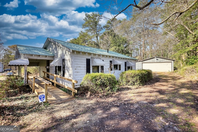 view of property exterior featuring metal roof, a detached garage, an outbuilding, and driveway