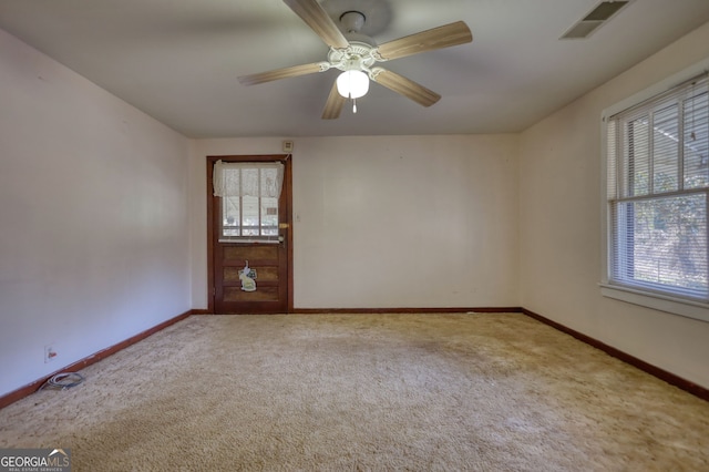 carpeted empty room featuring a wealth of natural light, visible vents, baseboards, and a ceiling fan