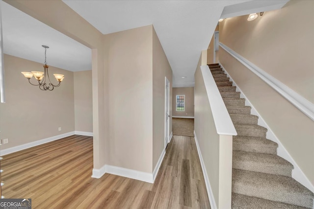 stairs featuring wood finished floors, baseboards, and a chandelier