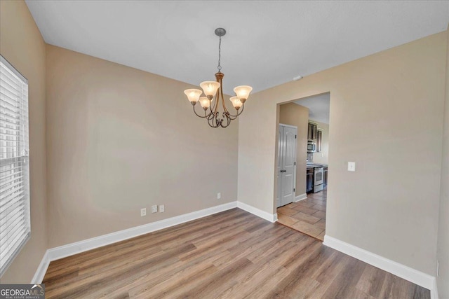 unfurnished room with wood finished floors, baseboards, and a chandelier