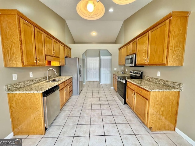 kitchen with light stone countertops, lofted ceiling, a sink, stainless steel appliances, and brown cabinets