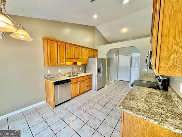 kitchen with brown cabinetry, light tile patterned flooring, a sink, vaulted ceiling, and appliances with stainless steel finishes