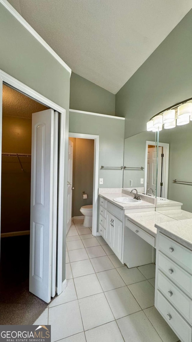 bathroom with tile patterned flooring, toilet, vanity, vaulted ceiling, and a textured ceiling