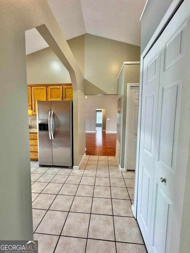 kitchen featuring light tile patterned flooring, stainless steel fridge, a textured ceiling, and baseboards