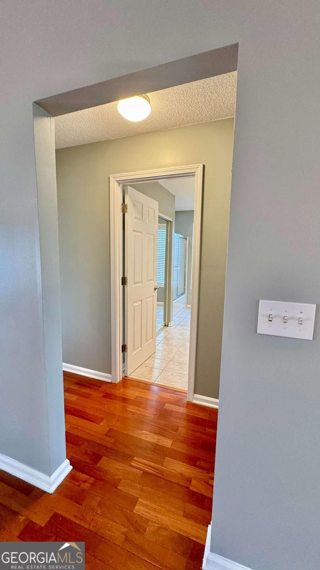 corridor featuring a textured ceiling, baseboards, and light wood-style floors