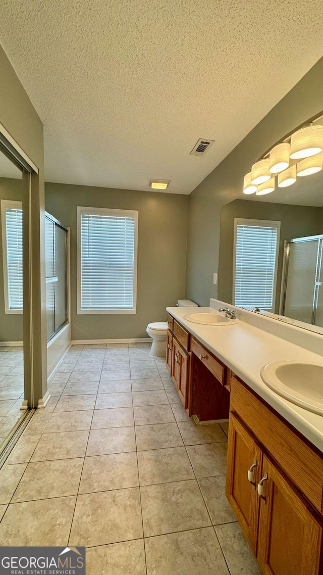 bathroom with tile patterned floors, a shower with shower door, visible vents, and a sink