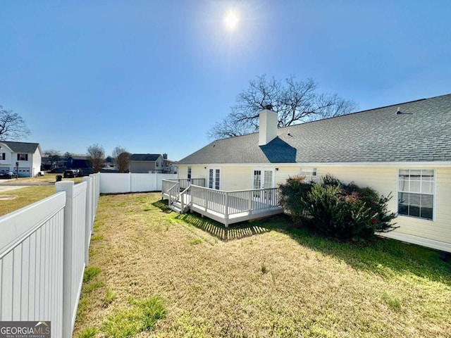 rear view of property featuring roof with shingles, a lawn, a chimney, a fenced backyard, and a deck