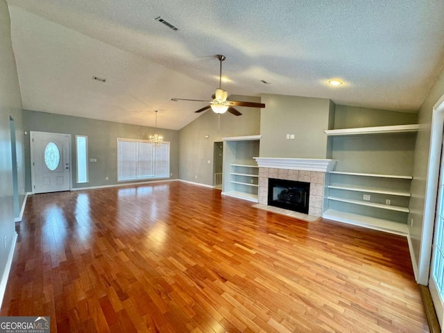 unfurnished living room featuring wood finished floors, visible vents, lofted ceiling, a tiled fireplace, and ceiling fan with notable chandelier