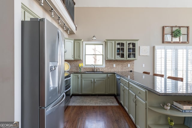 kitchen featuring dark wood-style floors, a peninsula, a sink, decorative backsplash, and appliances with stainless steel finishes