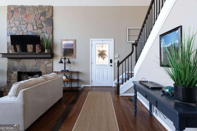 entrance foyer with stairs, a stone fireplace, wood finished floors, and baseboards