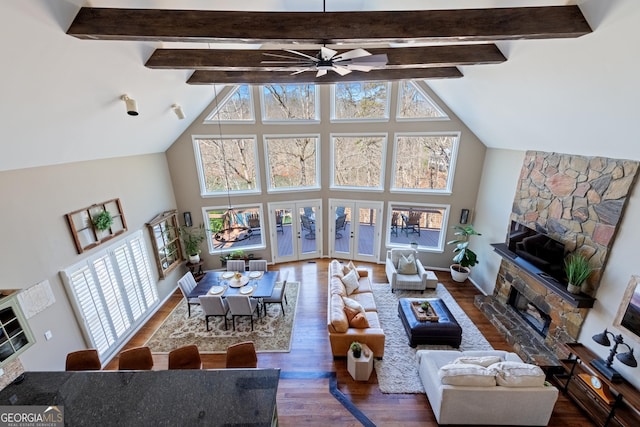 living area with a wealth of natural light, a stone fireplace, a ceiling fan, and wood finished floors