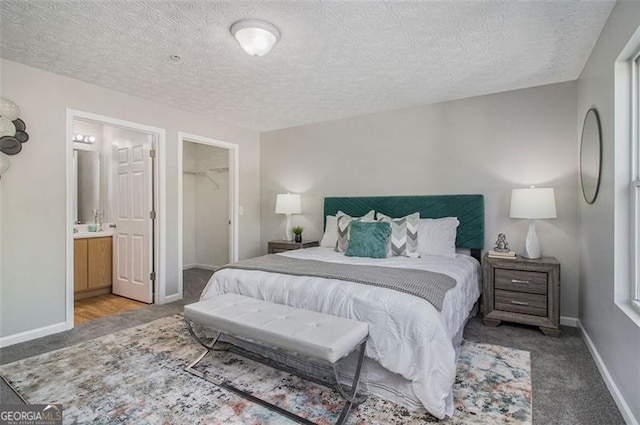 carpeted bedroom with a textured ceiling, baseboards, a walk in closet, and ensuite bath