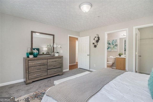 bedroom with baseboards, a spacious closet, carpet, a textured ceiling, and connected bathroom