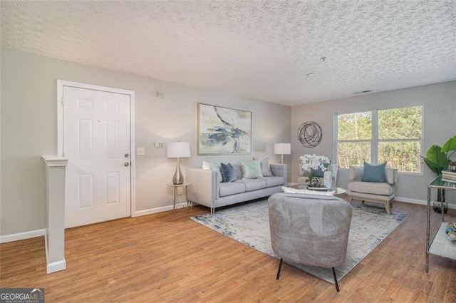living area with visible vents, light wood-style flooring, baseboards, and a textured ceiling