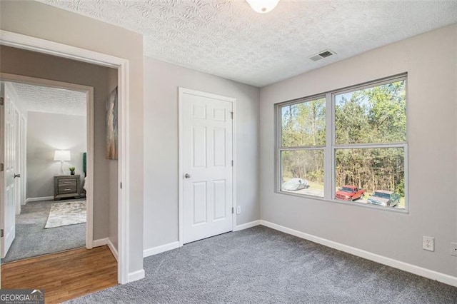 unfurnished bedroom featuring carpet, visible vents, baseboards, and a textured ceiling