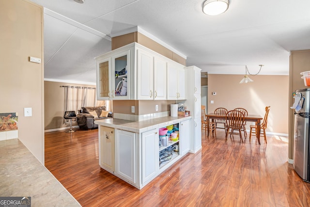 kitchen featuring glass insert cabinets, freestanding refrigerator, wood finished floors, hanging light fixtures, and white cabinetry