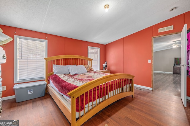 bedroom with visible vents, a textured ceiling, baseboards, and wood finished floors