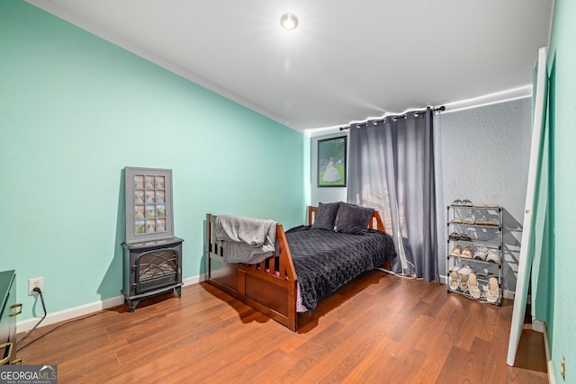 bedroom featuring a wood stove, wood finished floors, and baseboards