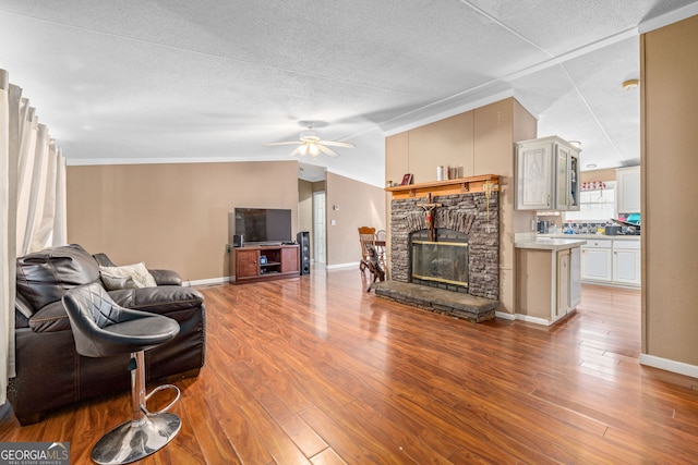 living area featuring lofted ceiling, wood finished floors, a stone fireplace, baseboards, and ceiling fan