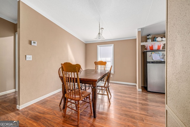 dining area featuring baseboards, a textured ceiling, wood finished floors, and a textured wall