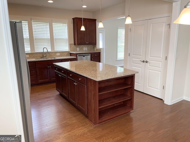 kitchen featuring a sink, open shelves, wood finished floors, appliances with stainless steel finishes, and a healthy amount of sunlight