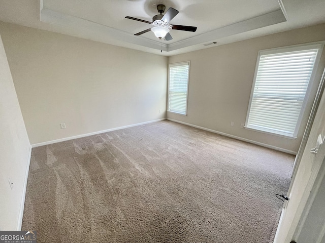 carpeted empty room with visible vents, baseboards, a tray ceiling, and a ceiling fan