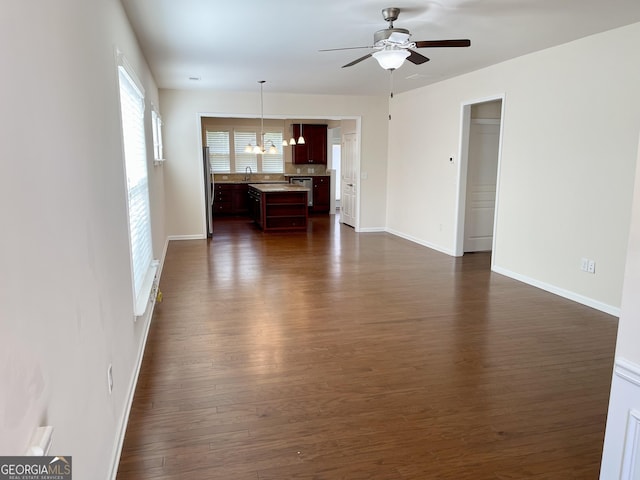 unfurnished living room with ceiling fan with notable chandelier, dark wood-style floors, baseboards, and a sink