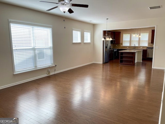 unfurnished living room featuring visible vents, dark wood-type flooring, baseboards, a ceiling fan, and a sink