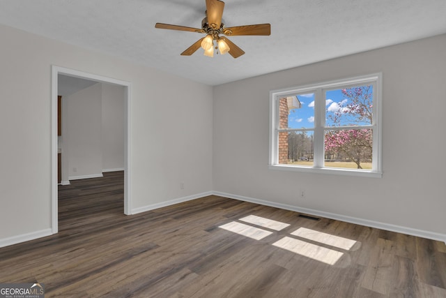 empty room with dark wood-style floors, visible vents, baseboards, ceiling fan, and a textured ceiling