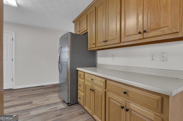 kitchen with light wood finished floors, a textured ceiling, freestanding refrigerator, light countertops, and baseboards