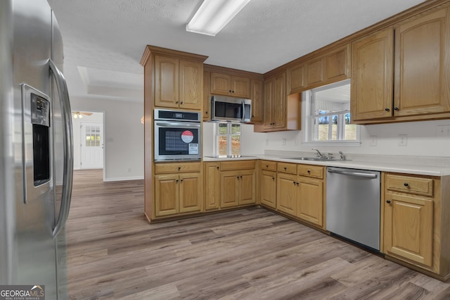 kitchen featuring light wood-type flooring, a sink, a tray ceiling, appliances with stainless steel finishes, and light countertops