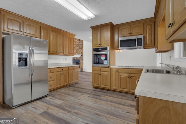 kitchen featuring light wood-style flooring, a sink, light countertops, appliances with stainless steel finishes, and a textured ceiling