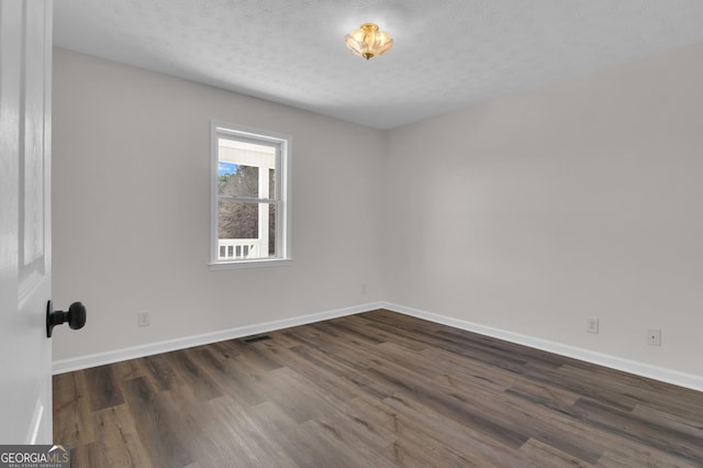 empty room with dark wood-type flooring, baseboards, visible vents, and a textured ceiling