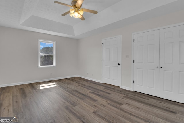 unfurnished bedroom featuring a ceiling fan, wood finished floors, baseboards, a closet, and a raised ceiling