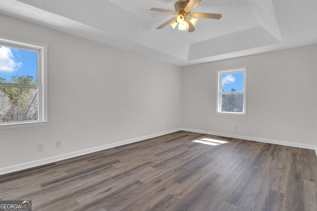 empty room featuring a ceiling fan, baseboards, dark wood finished floors, a tray ceiling, and a textured ceiling