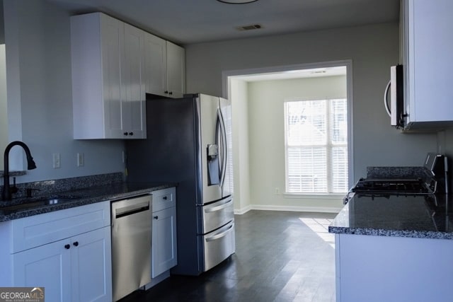 kitchen featuring dark stone countertops, dark wood finished floors, a sink, stainless steel appliances, and white cabinets