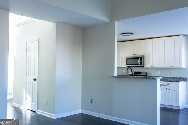 kitchen featuring stainless steel microwave, baseboards, dark wood-style floors, and white cabinetry