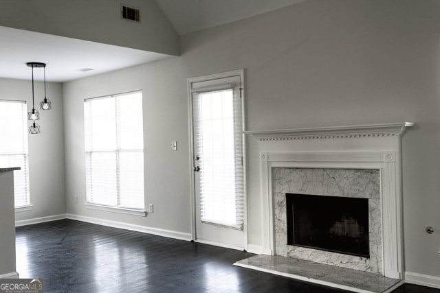 unfurnished living room featuring visible vents, baseboards, vaulted ceiling, a premium fireplace, and dark wood-style floors