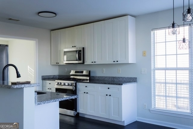 kitchen featuring visible vents, decorative light fixtures, dark stone countertops, white cabinets, and stainless steel appliances