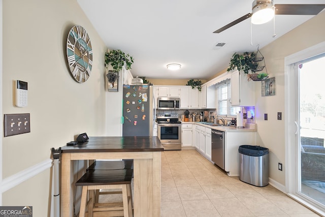 kitchen featuring tasteful backsplash, light tile patterned floors, white cabinets, stainless steel appliances, and a ceiling fan